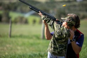 Youth assited by instructors hit moving clay targets with shotguns